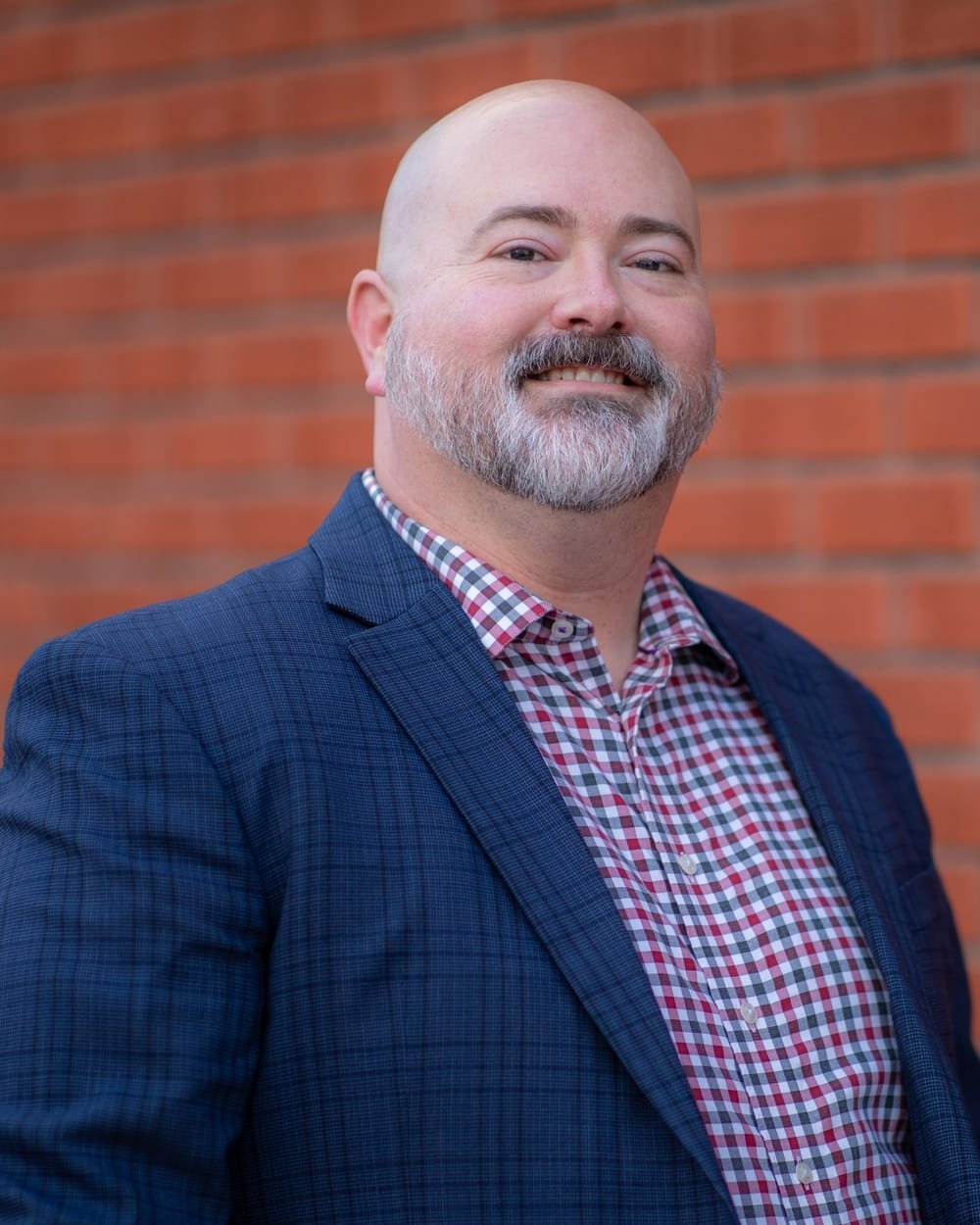 Adam Broadbent, CTO of MadeLabs, in a blue blazer and check shirt in front of a red brick wall