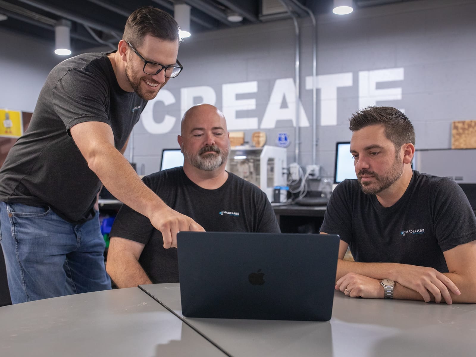 A MadeLabs engineer points at a laptop screen while Adam Broadbent and Nicholas Barger follow along in the MadeLabs office